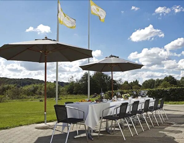 Un espacio para comer al aire libre con mesas, sillas, dos sombrillas y banderas.