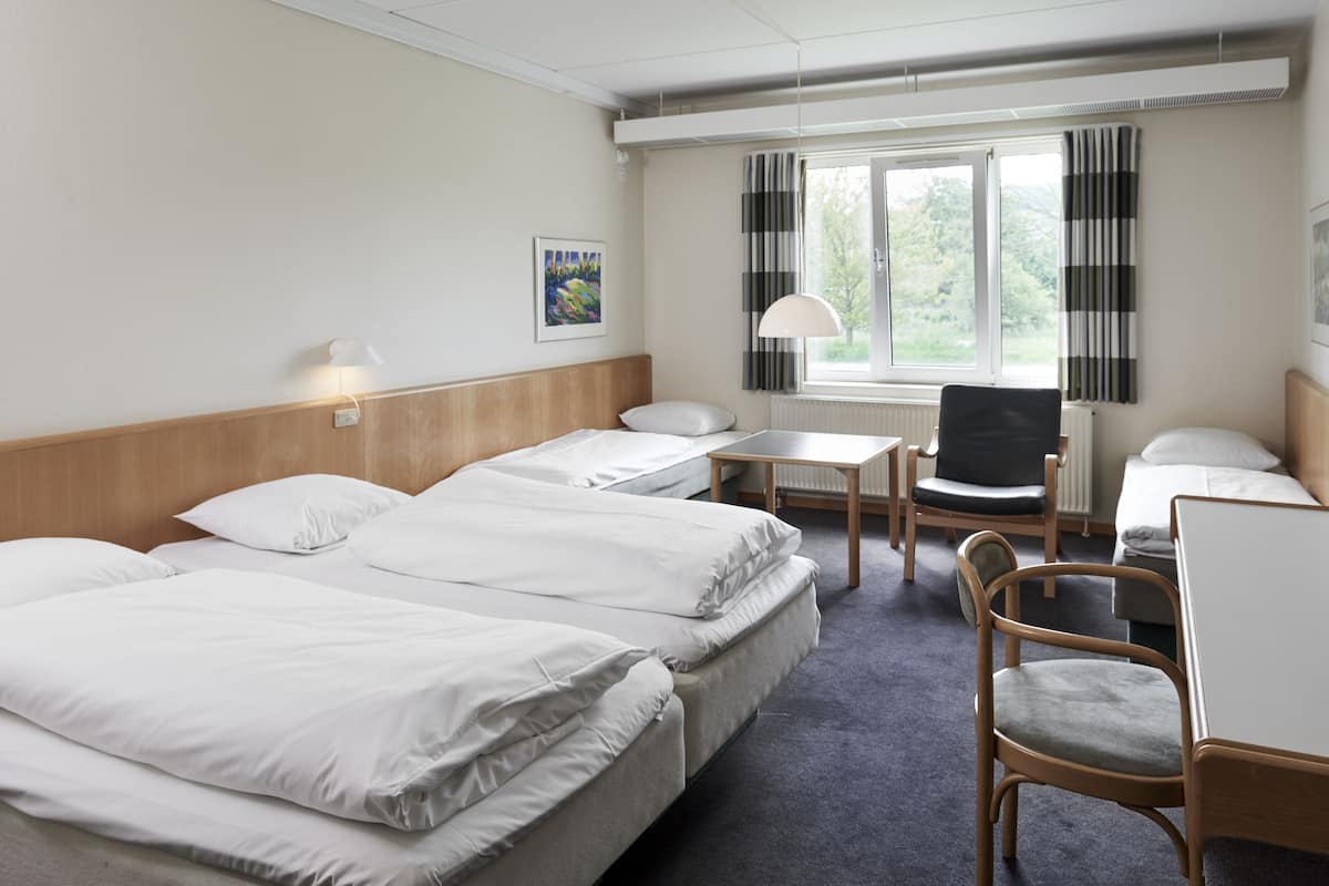 A hotel room with three beds, a desk, a chair, and a window with curtains.
