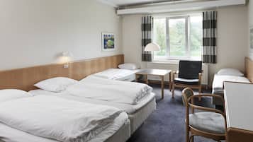Een hotelkamer met drie bedden, een bureau, een stoel en een raam met gordijnen.