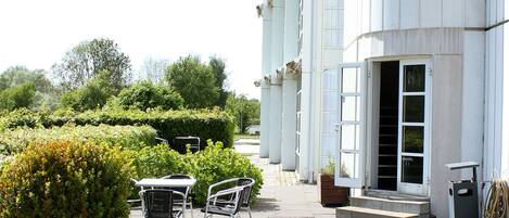 An outdoor patio area with a large potted plant, outdoor furniture, and a building with large windows and a door.