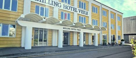 A hotel with a name sign, a covered entrance, and outdoor seating.