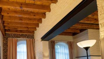 A room with exposed wooden beams, brick walls, and large windows with curtains.