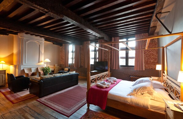 A room with a four-poster bed, a sofa, a television, and a fireplace.