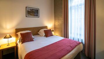 A hotel room with a large bed, two bedside lamps, a framed picture on the wall, and a window with curtains.
