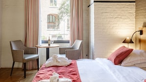 Una habitación de hotel con una cama, dos sillones, una mesita y una ventana con cortinas.