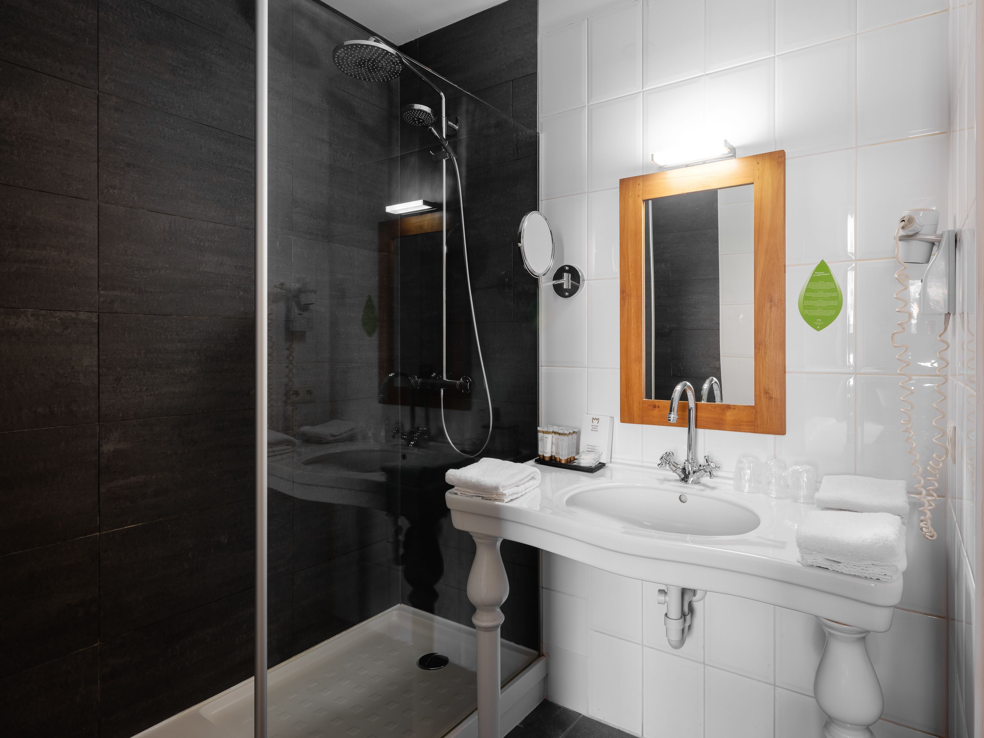 A modern bathroom with a glass-enclosed shower, a white sink with a wooden frame mirror, and a white toilet.