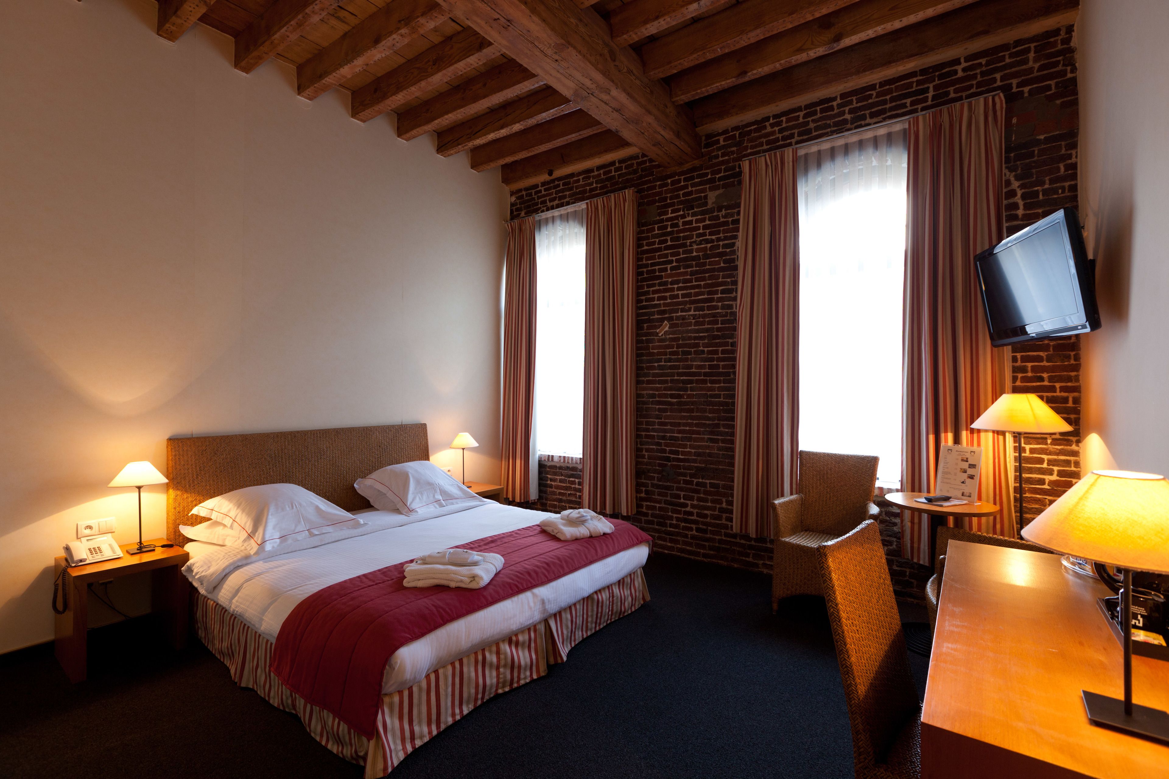 Une chambre d’hôtel avec un lit, un bureau, une chaise, une télévision et une lampe.