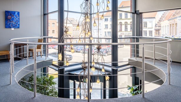 Un interior moderno con una escalera circular de paredes de vidrio, un candelabro colgante y vistas de la ciudad.