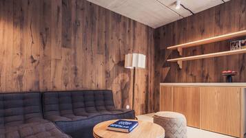 Una habitación moderna con una pared de madera, un sofá, una mesa redonda con un libro, una lámpara y un pequeño otoman.