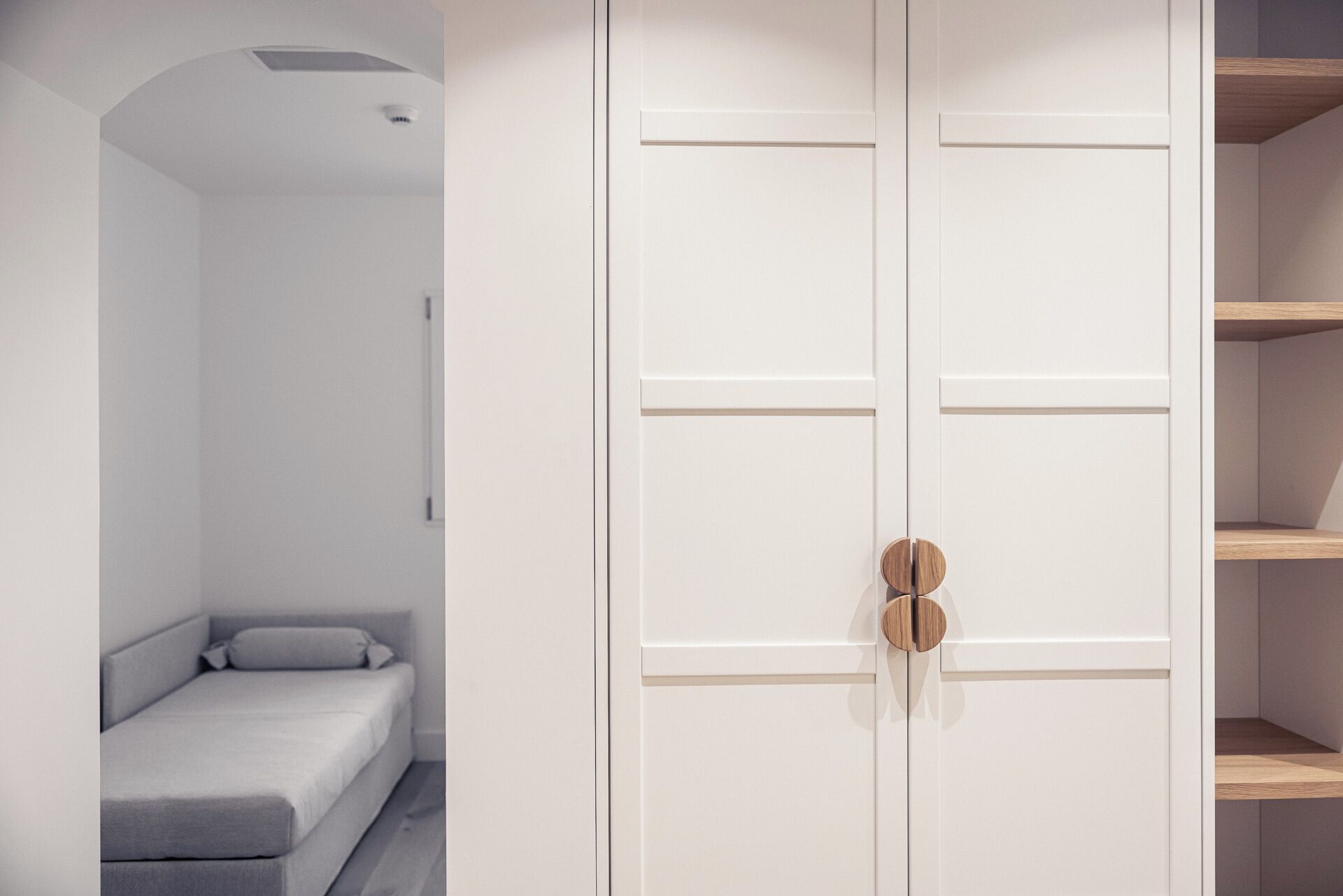 A minimalist room with a large white wardrobe, a grey sofa, and a small bed.