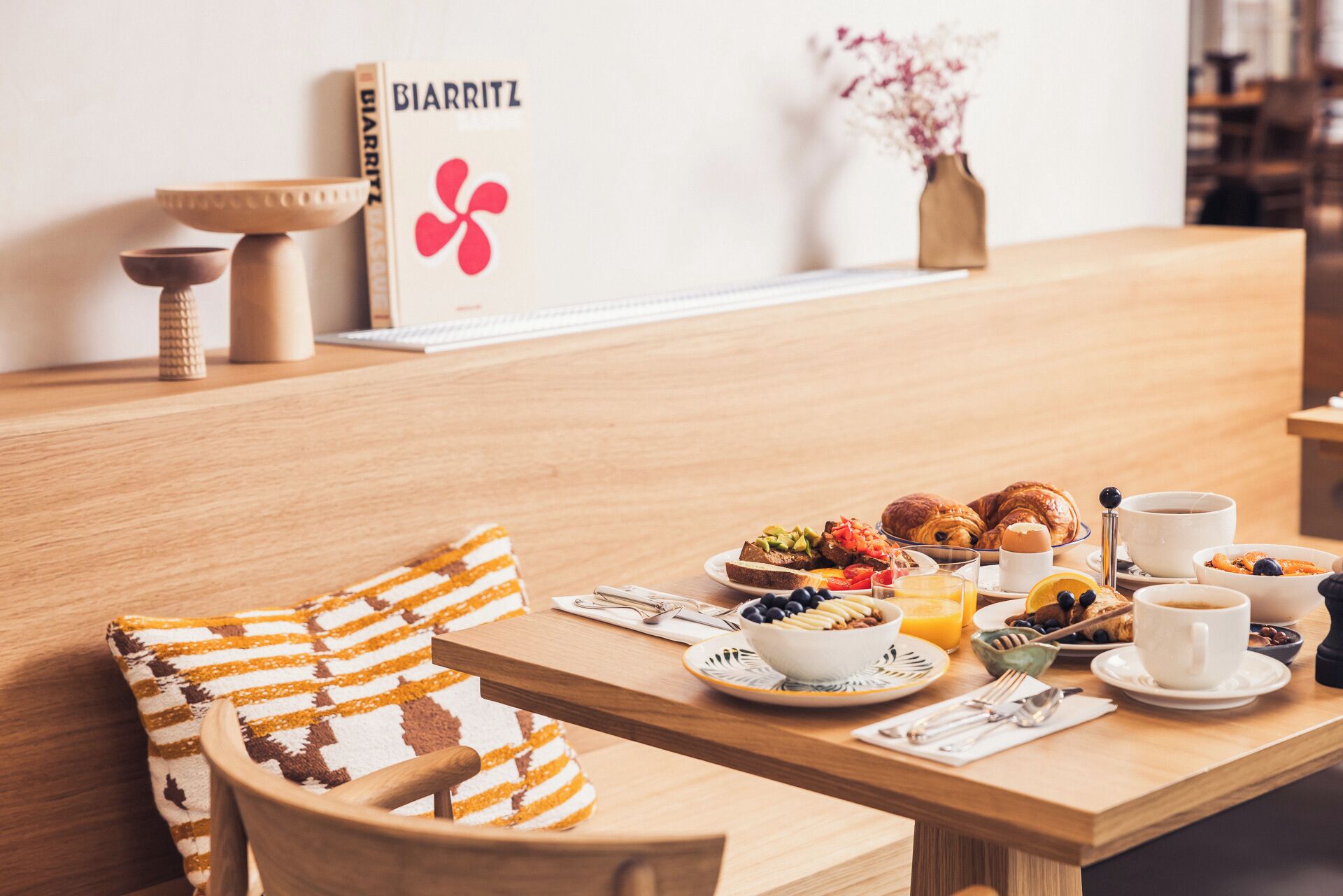 Desayuno con una mesa de madera, un bol de fruta, croissants y una taza de café.