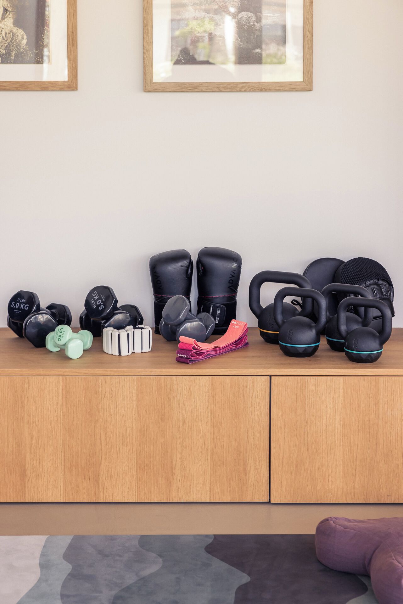 A wooden cabinet with various fitness equipment including dumbbells, kettlebells, and resistance bands.