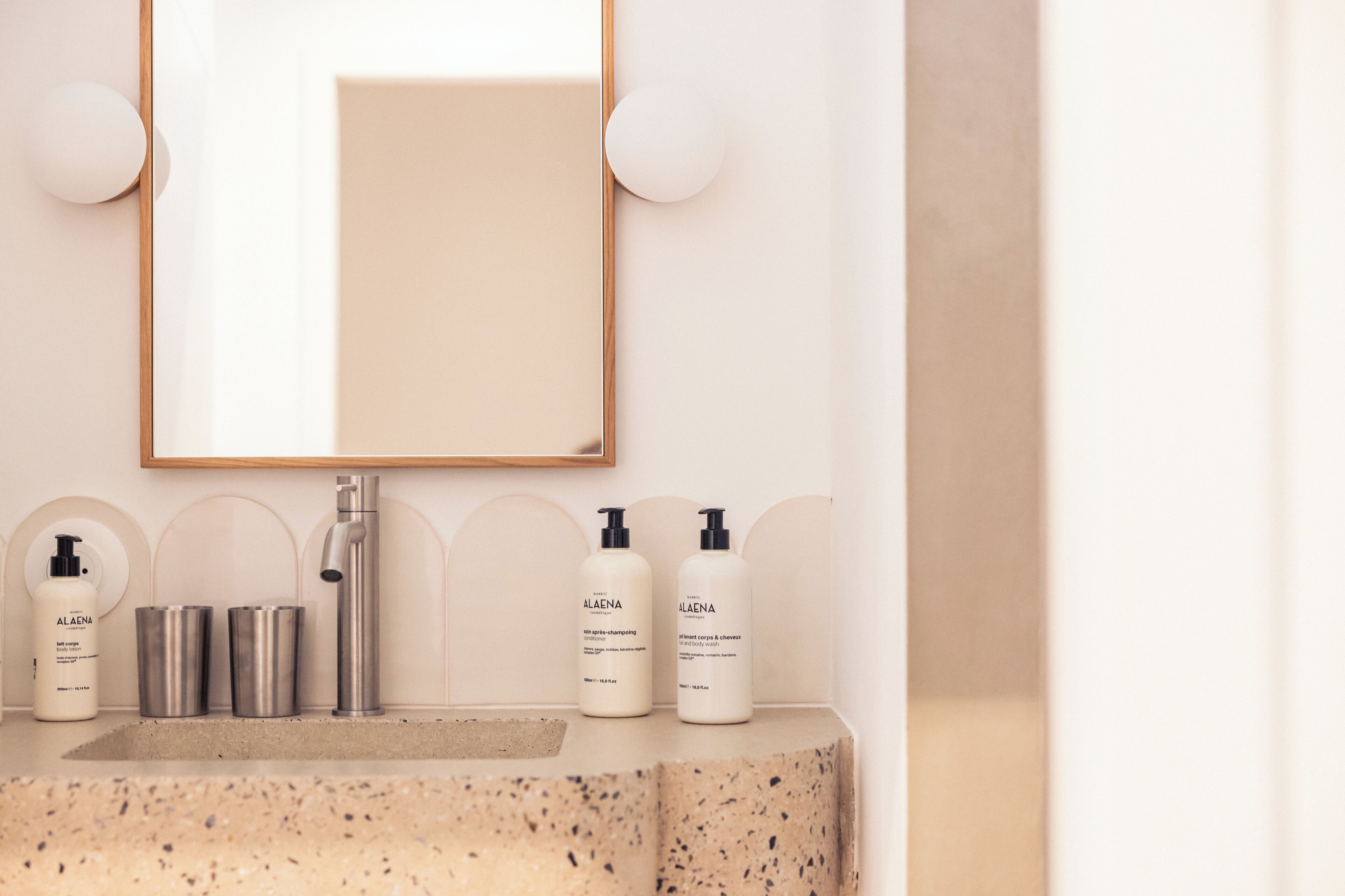 Un baño con una encimera con vetas, un espejo y dos botellas de productos para el cuidado de la piel ALAENA.