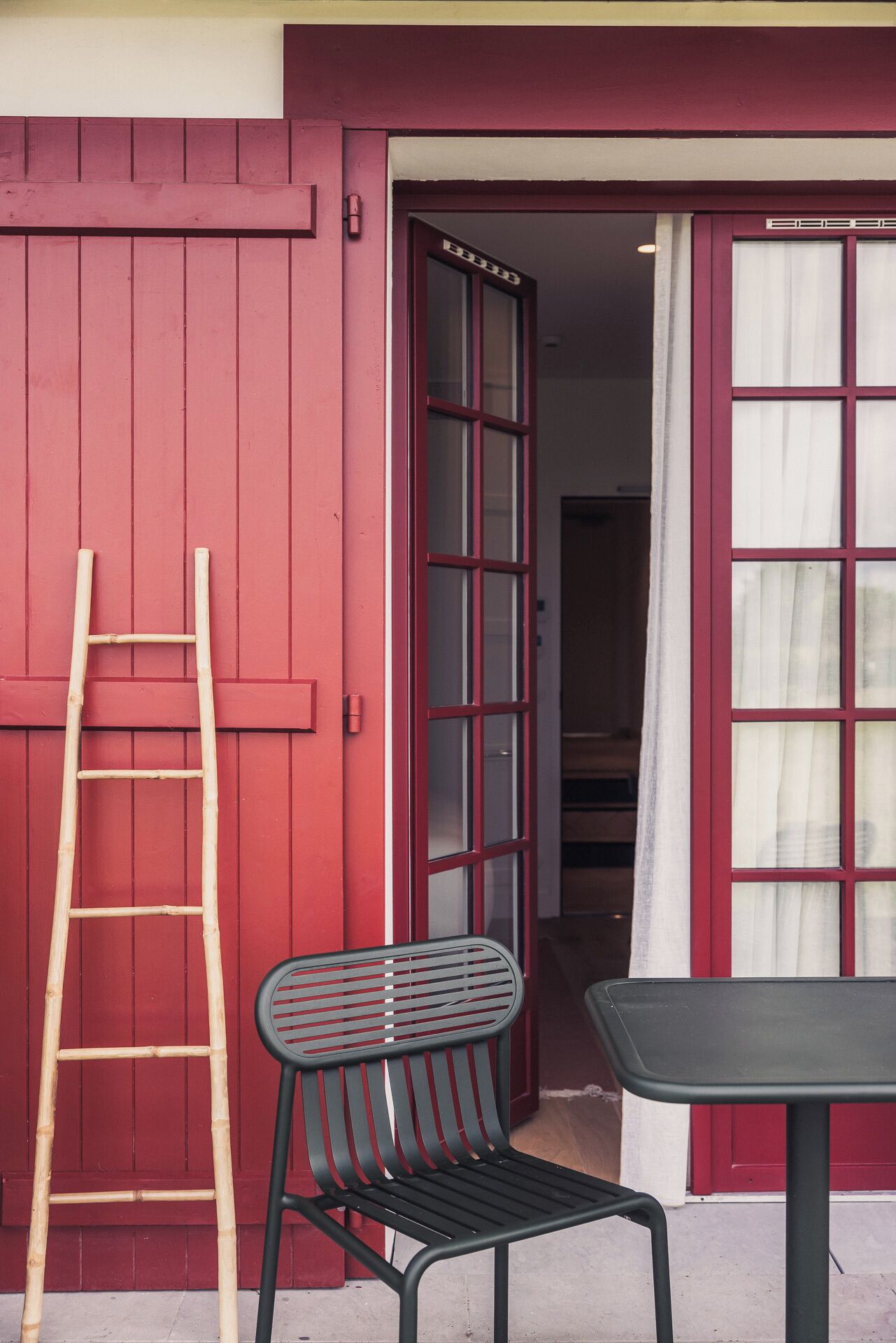 Une porte rouge avec une fenêtre, une échelle en bois et une chaise en métal à l’extérieur.