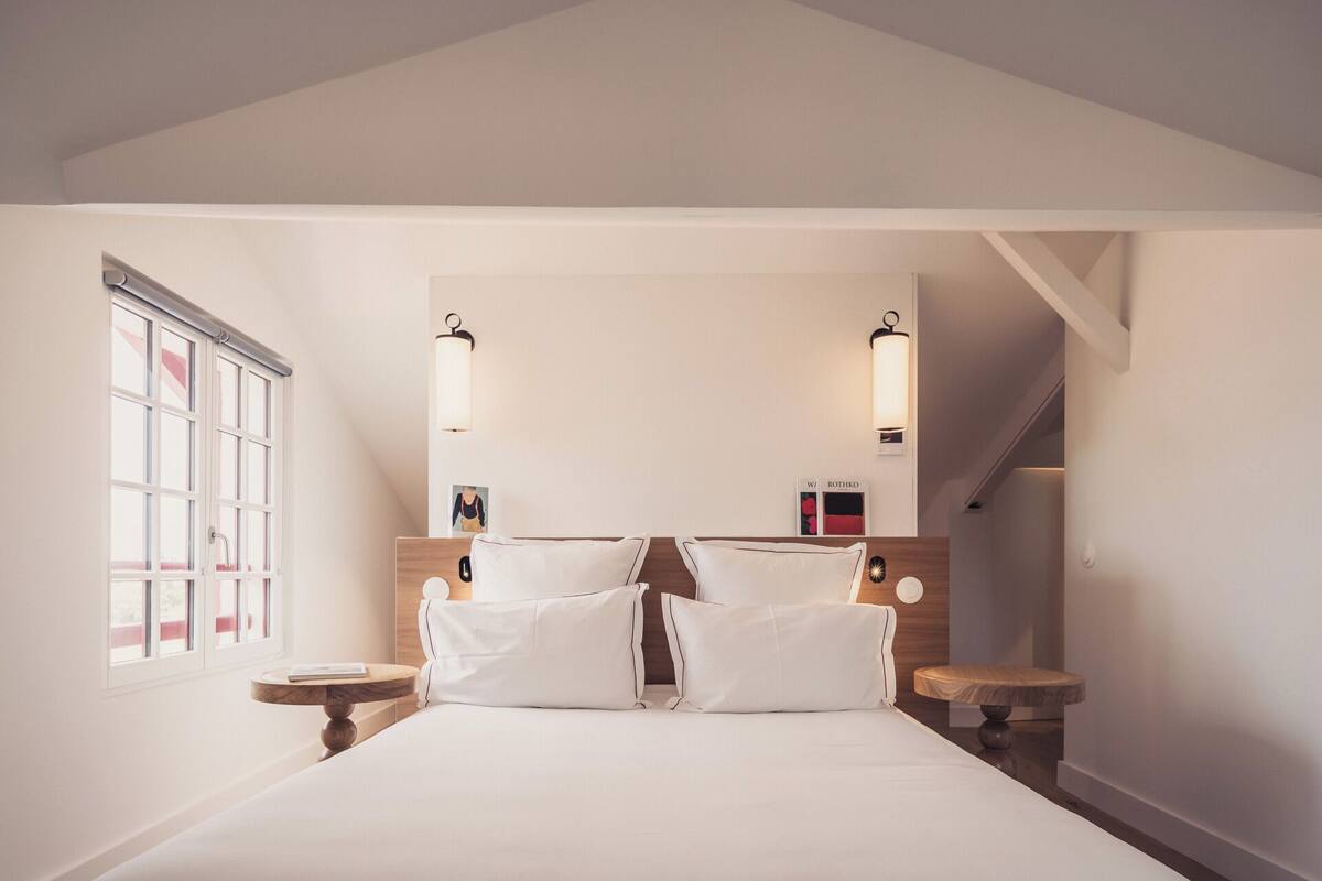 Une chambre à coucher avec un grand lit, deux tables de chevet, une tête de lit en bois et une fenêtre avec des stores.
