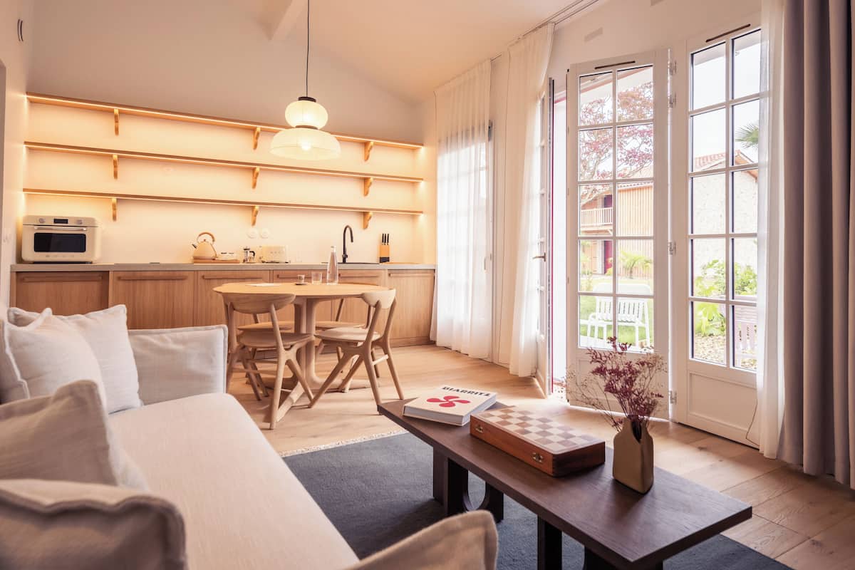 Un salon moderne comprenant un canapé, une table à manger et un coin cuisine avec des étagères en bois et un four à micro-ondes.