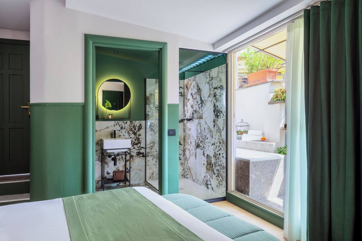 A modern bedroom with a bed, a bathroom with a marble wall, and a view of the outside.