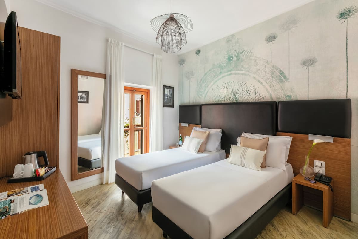 A hotel room with two beds, a wooden desk, a mirror, a wall mural, and a hanging light fixture.