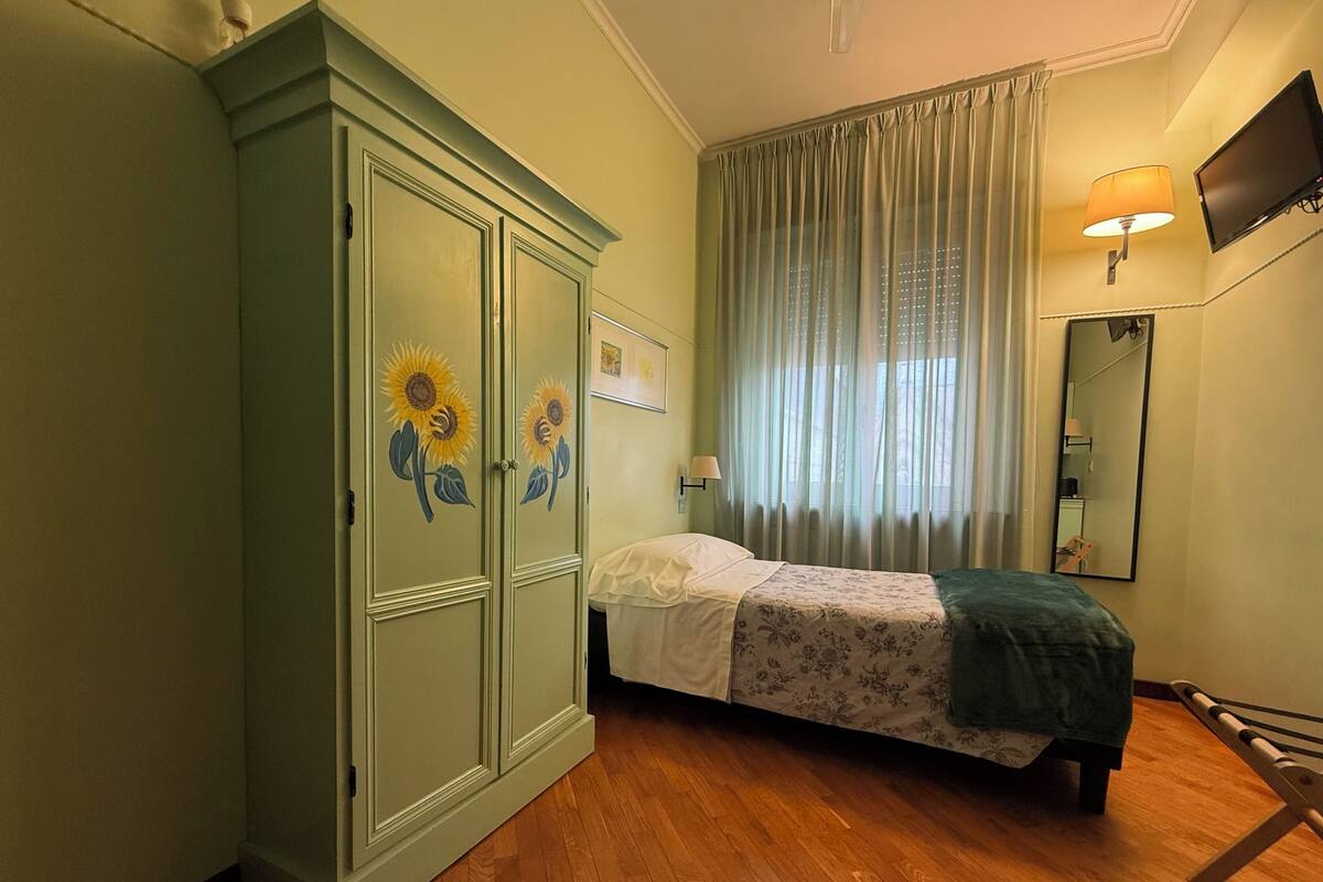 Une chambre à coucher avec un lit, une armoire décorée de motifs de tournesols, une fenêtre avec des rideaux, une lampe de chevet et un téléviseur fixé au mur.
