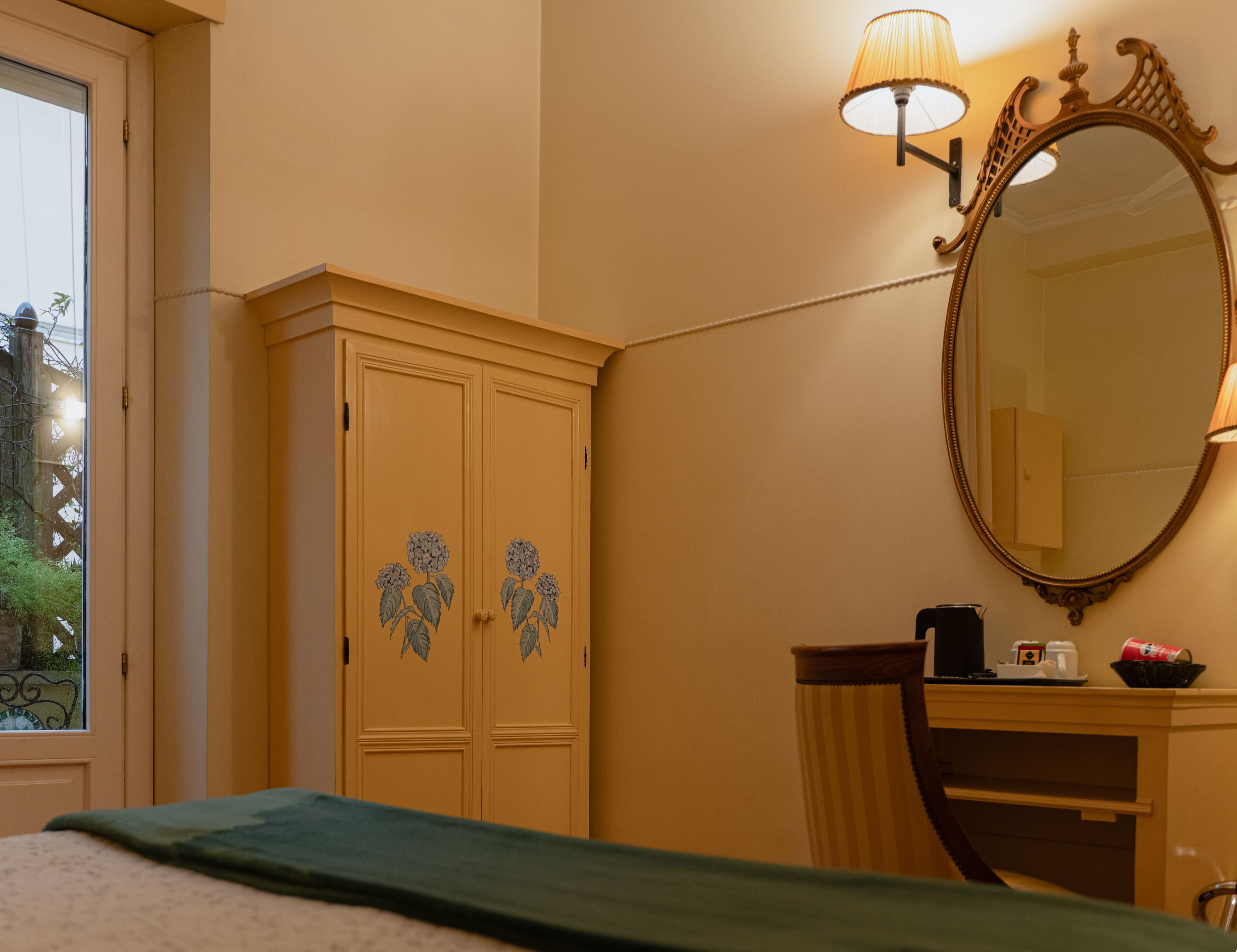 A bedroom with a bed, a wardrobe with floral designs, a mirror, and a bedside table with a lamp.