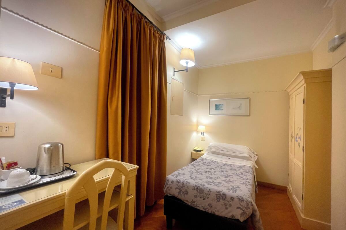Une chambre d’hôtel comprenant un lit, un bureau, une chaise, une armoire et une table de chevet avec une lampe.