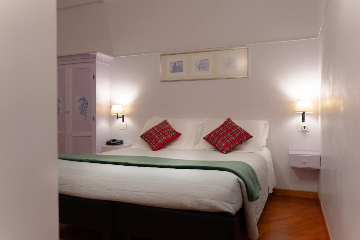 Une chambre à coucher bien rangée, avec un lit, des lampes de chevet, une table de nuit, une armoire et des œuvres d’art encadrées accrochées au mur.