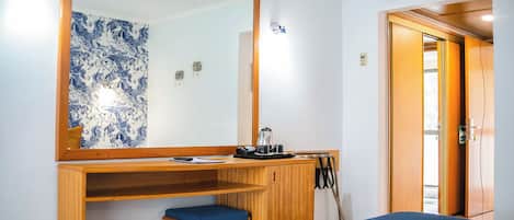 Habitación de hotel con un escritorio de madera, un espejo grande, una cama con manta azul y una puerta que da a otra habitación.