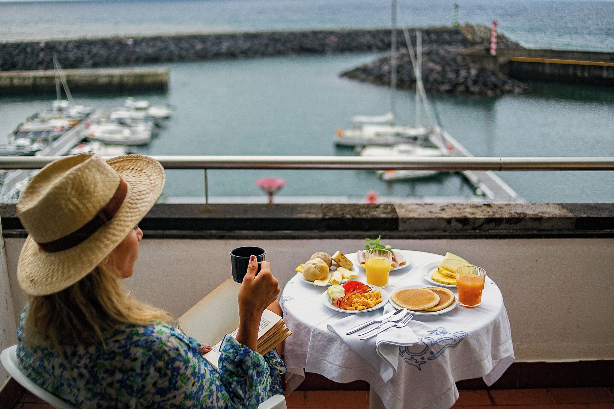 A person seated at a table with a meal, overlooking a marina with boats.