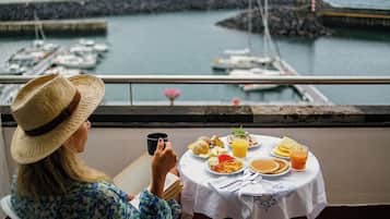 A person seated at a table with a meal, overlooking a marina with boats.