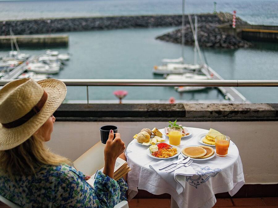 A person seated at a table with a meal, overlooking a marina with boats.