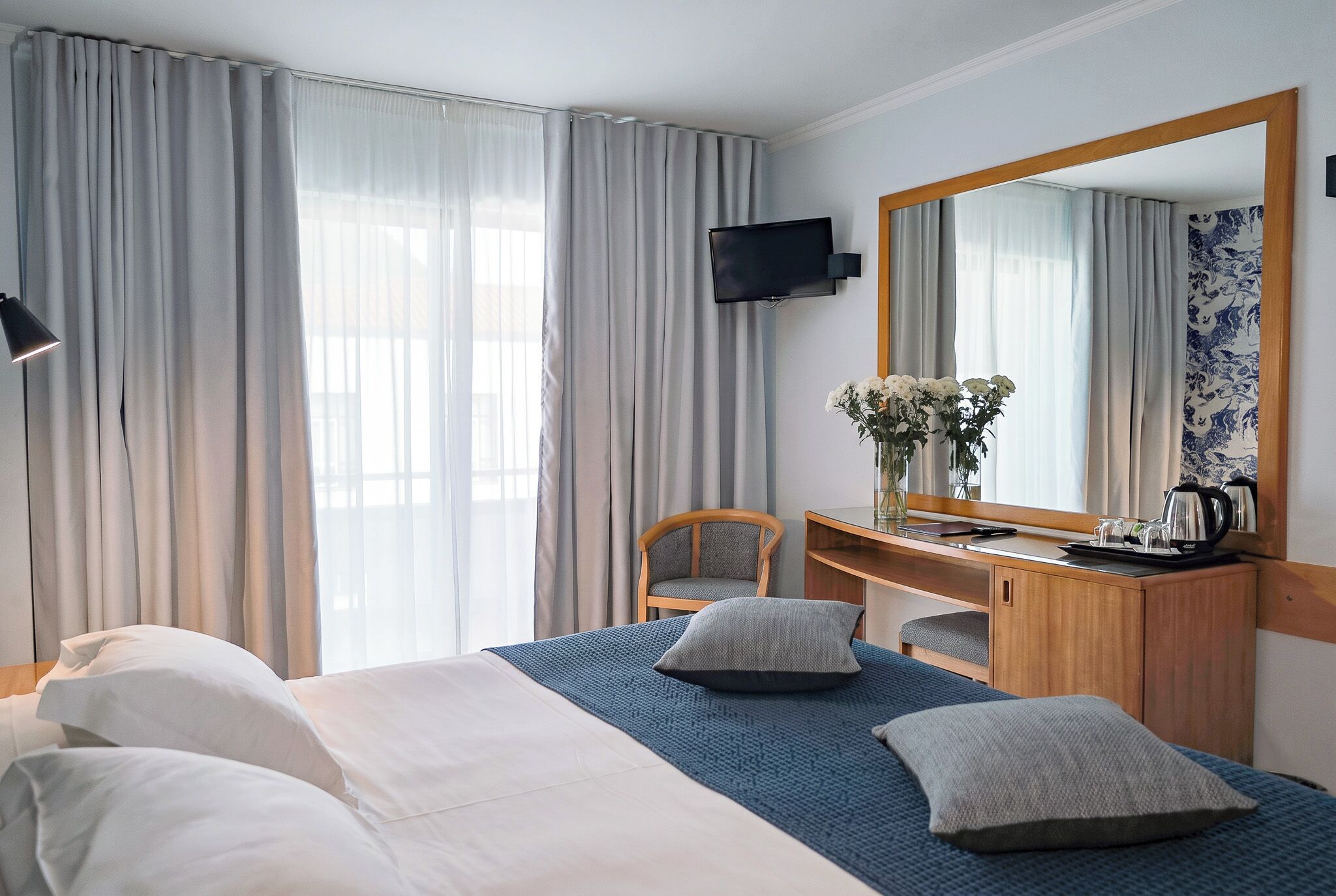 A hotel room with a bed, a desk, a chair, a television, and a large mirror.