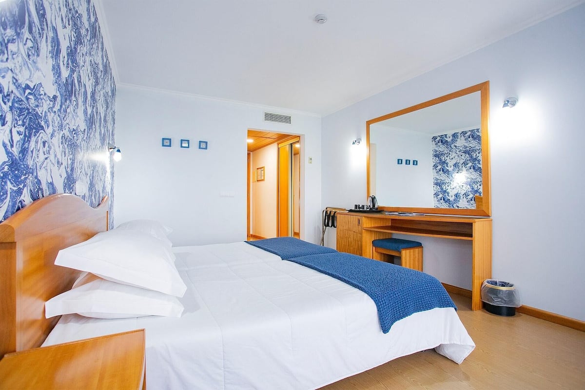 A hotel room with a bed, a desk, a mirror, and a bathroom door.