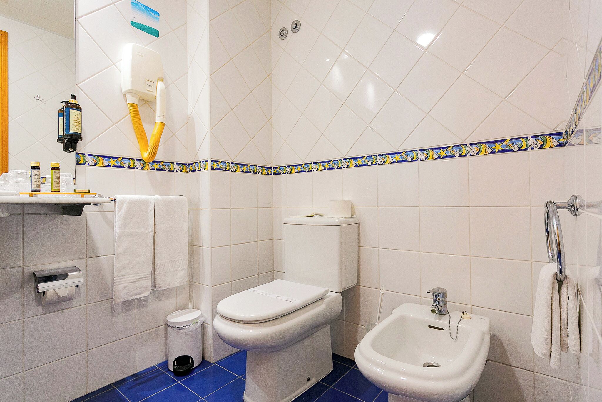 A bathroom with a toilet, bidet, and sink, with a blue floor and decorative tiles.