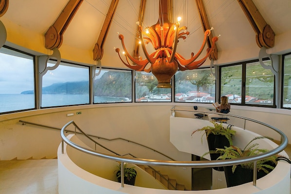 A high-ceilinged interior with a central chandelier, a curved staircase, and a view of the sea through large windows. - Hotel do Mar (Povoacao)