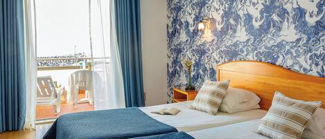 A hotel room with a bed, a nightstand, a window with curtains, and a view of the outside.