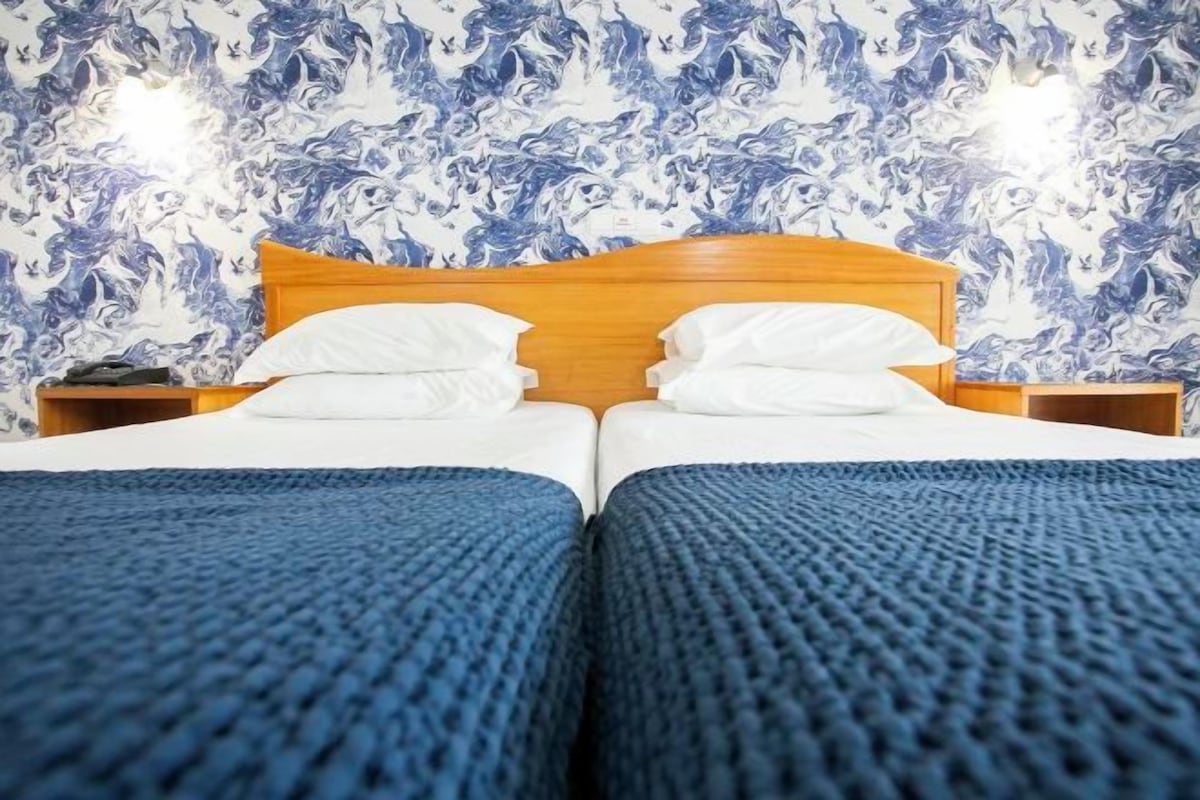 A double bed with a wooden headboard, two white pillows, and a blue textured blanket.