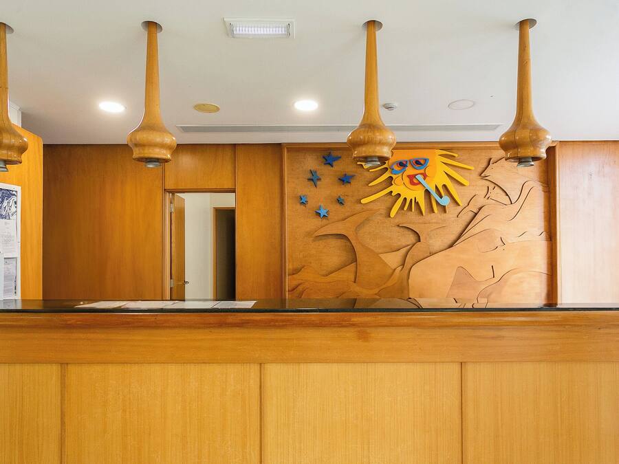 A reception desk with wooden paneling, a wall-mounted sun decoration, and pendant lights.