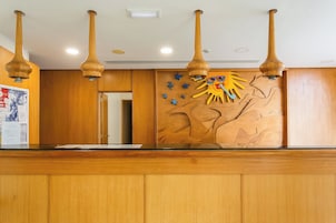 Un mostrador de recepción con paneles de madera, un adorno de sol en la pared y luces colgantes.