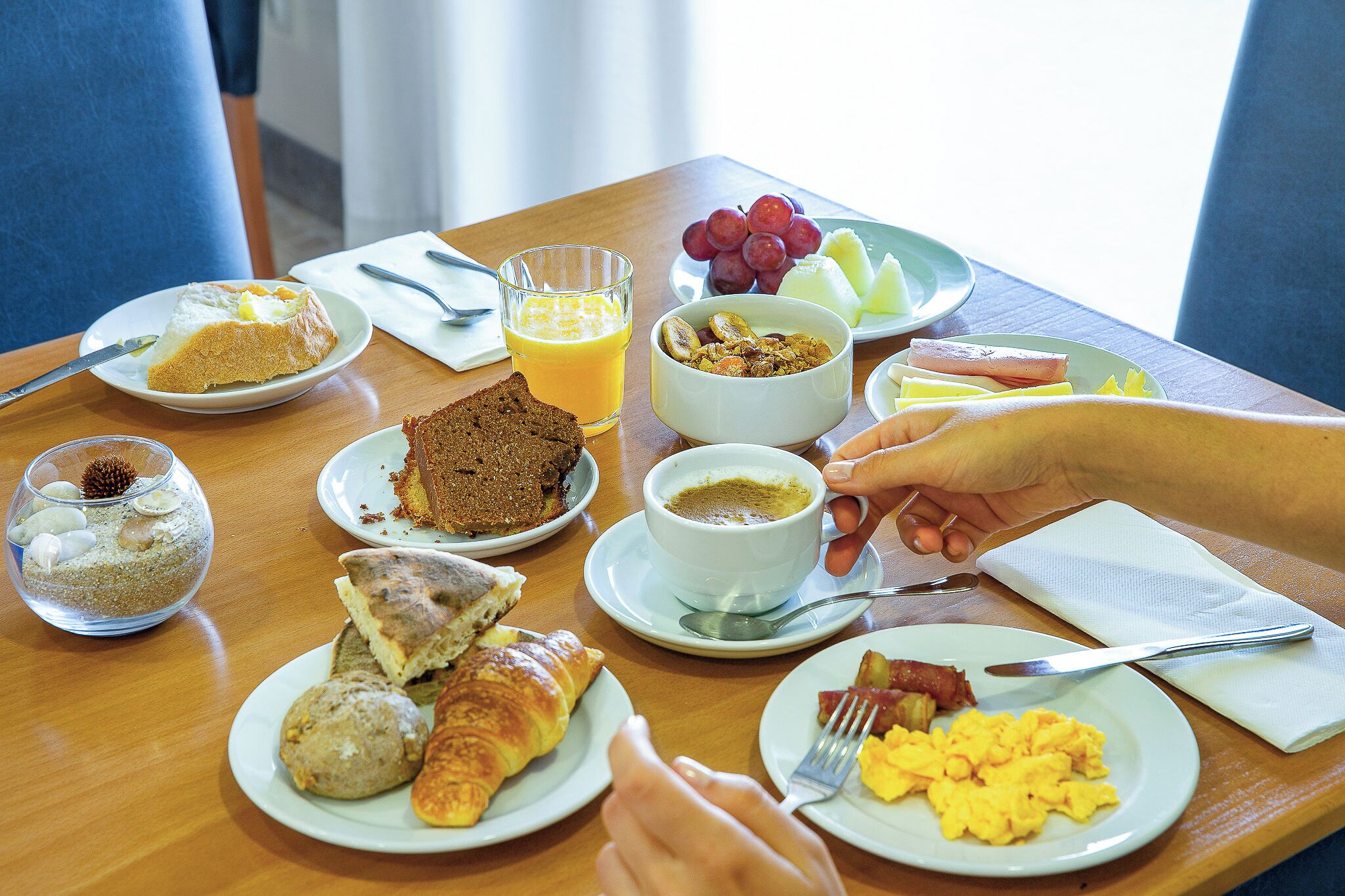 A breakfast table with various dishes including toast, croissants, scrambled eggs, and a glass of orange juice.