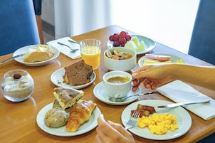 Una mesa de desayuno con diversos platos, incluyendo tostadas, croissants, huevos revueltos y un vaso de jugo de naranja.