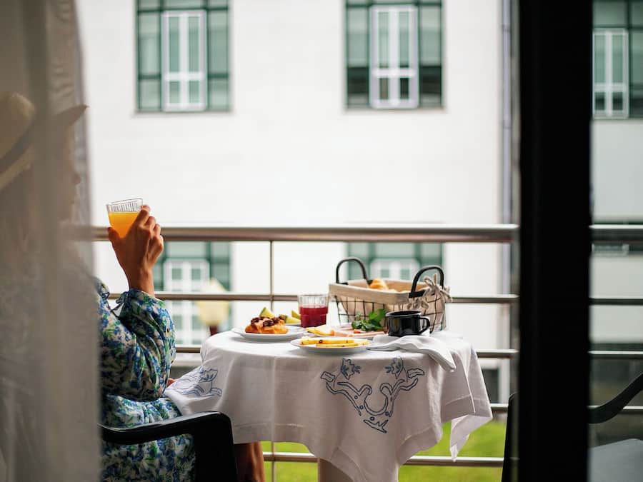 Henkilö istuu pöydän ääressä, ja hänen edessään on juoma, kori täynnä leivonnaisia ja lautanen ruokaa.