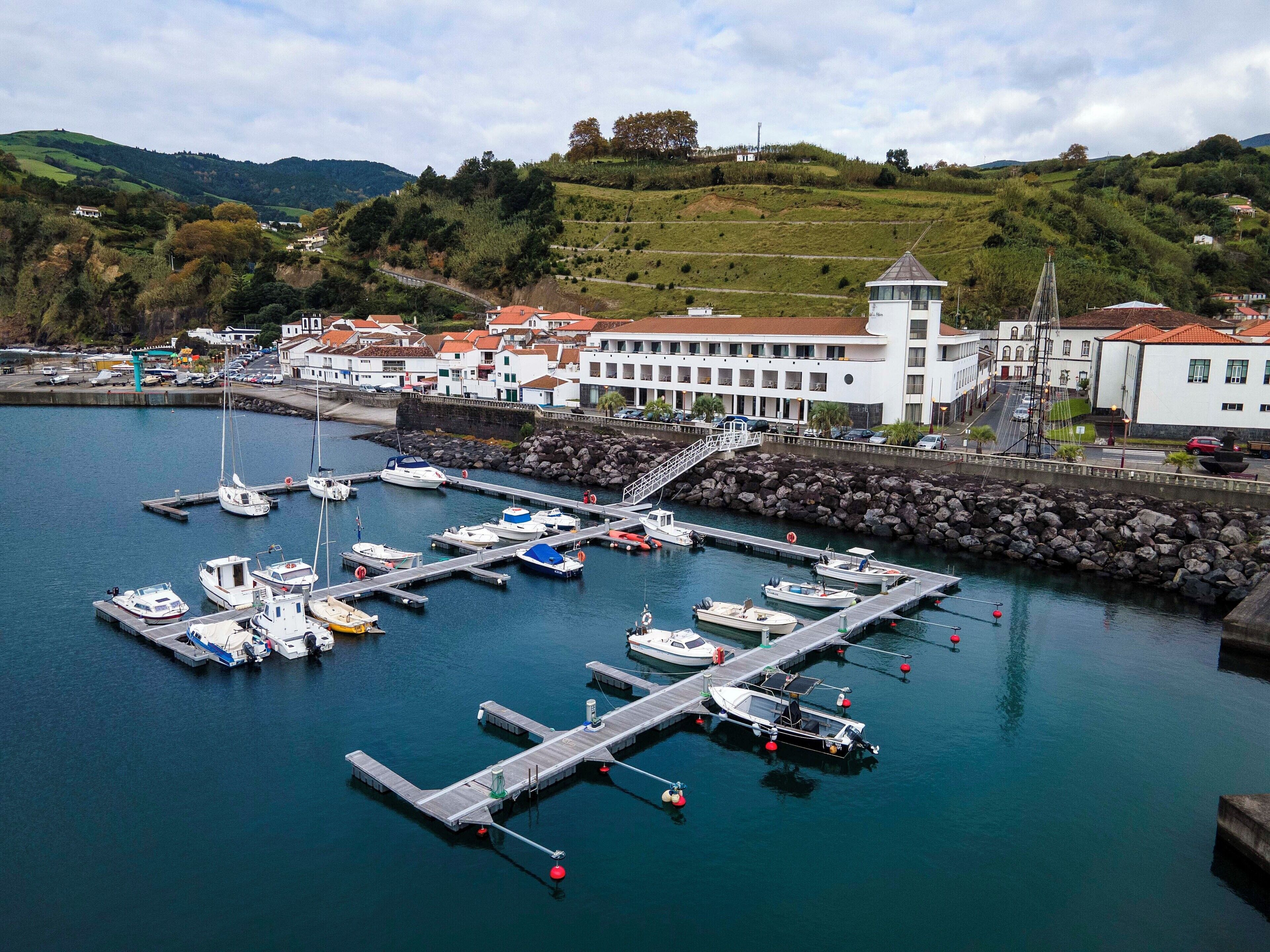 A marina with boats docked, a white building with a red roof, and a hill in the background.