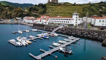 A marina with boats docked, a white building with a red roof, and a hill in the background.