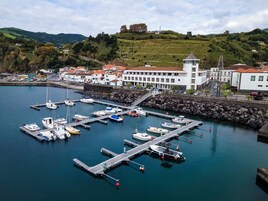 Un puerto deportivo con barcos amarrados, un edificio blanco de techo rojo y una colina al fondo.