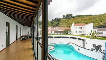 A view of a swimming pool from a covered balcony with exercise equipment visible.