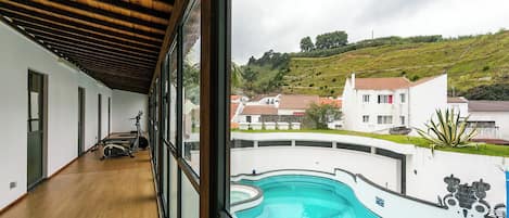 Vista de una piscina desde un balcón techado, con equipo de ejercicio a la vista.