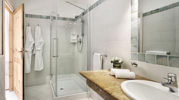 Une salle de bain moderne dotée d’une douche à parois de verre, d’un comptoir en granit, d’un lavabo et d’un miroir.