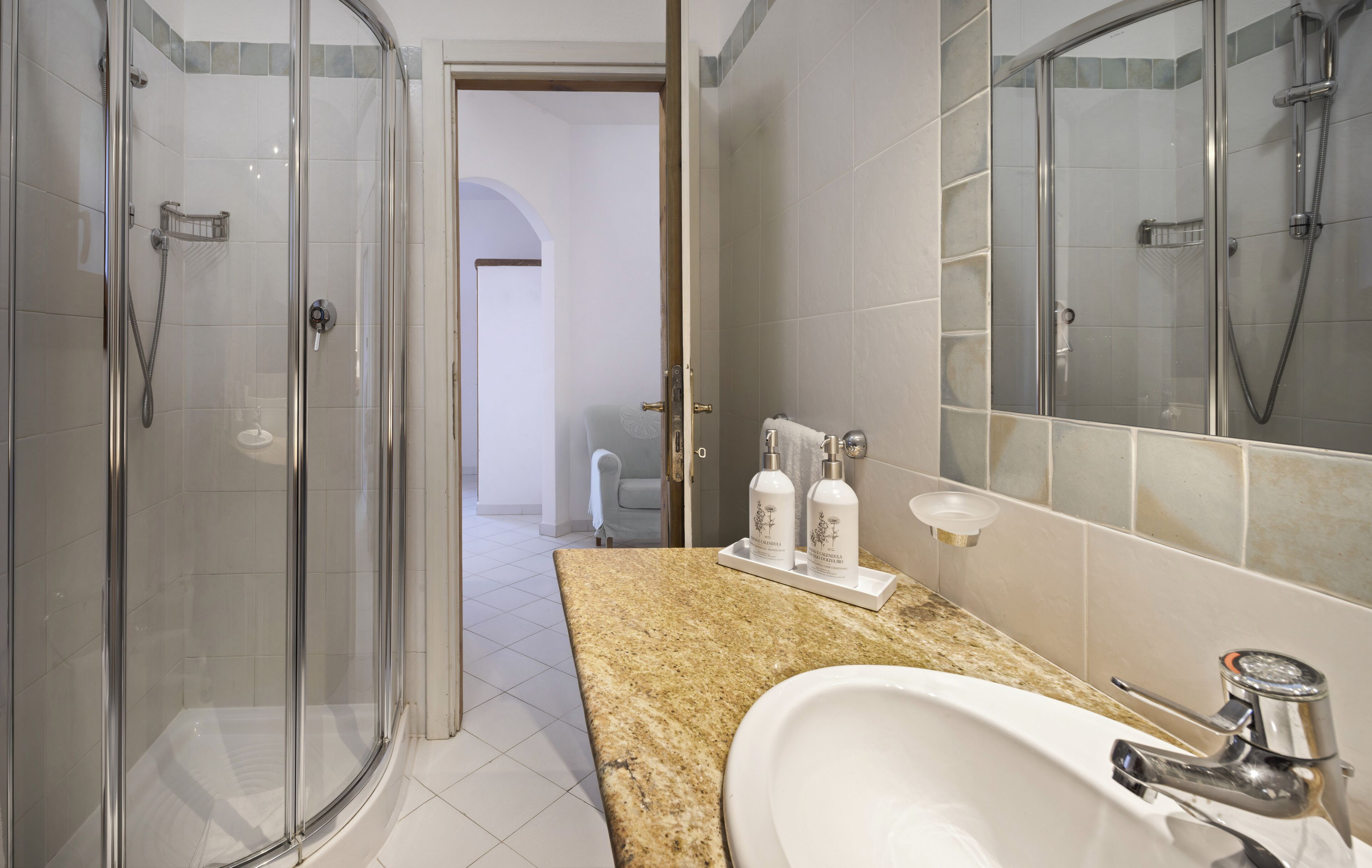 A bathroom with a glass-enclosed shower, a sink with a chrome faucet, and a countertop with toiletries.