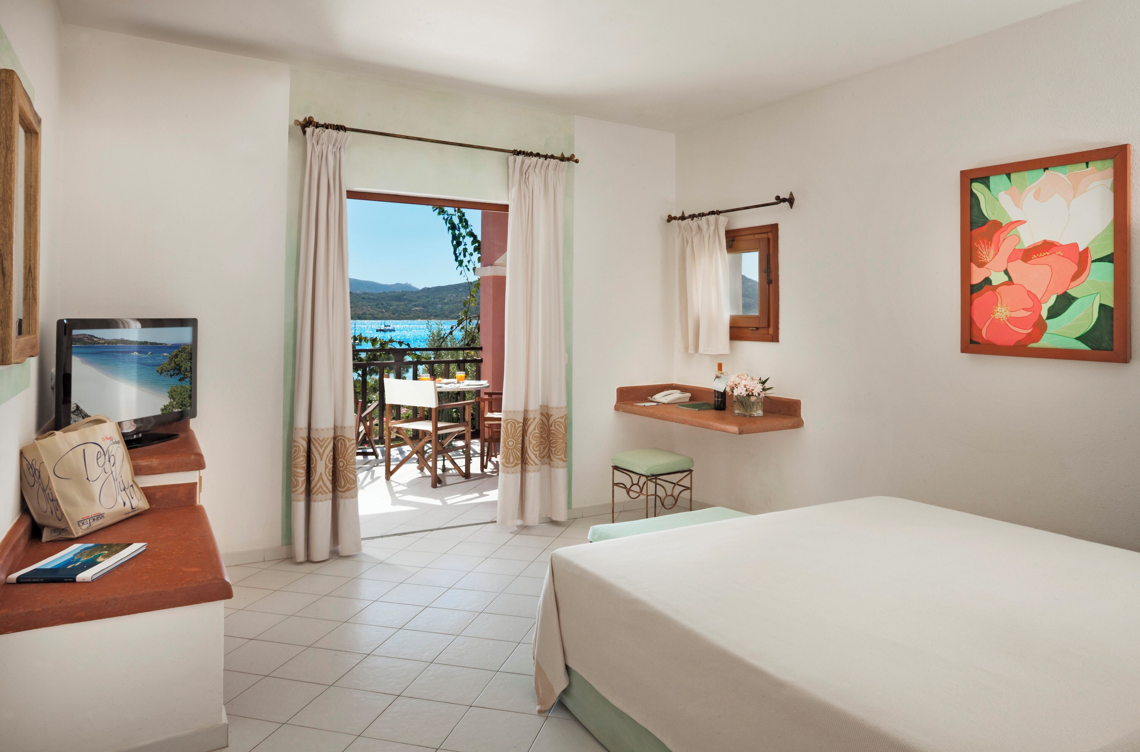 Une chambre d’hôtel avec un lit, un bureau avec un ordinateur, une chaise, une petite table, une fenêtre avec des rideaux et une vue sur la mer.