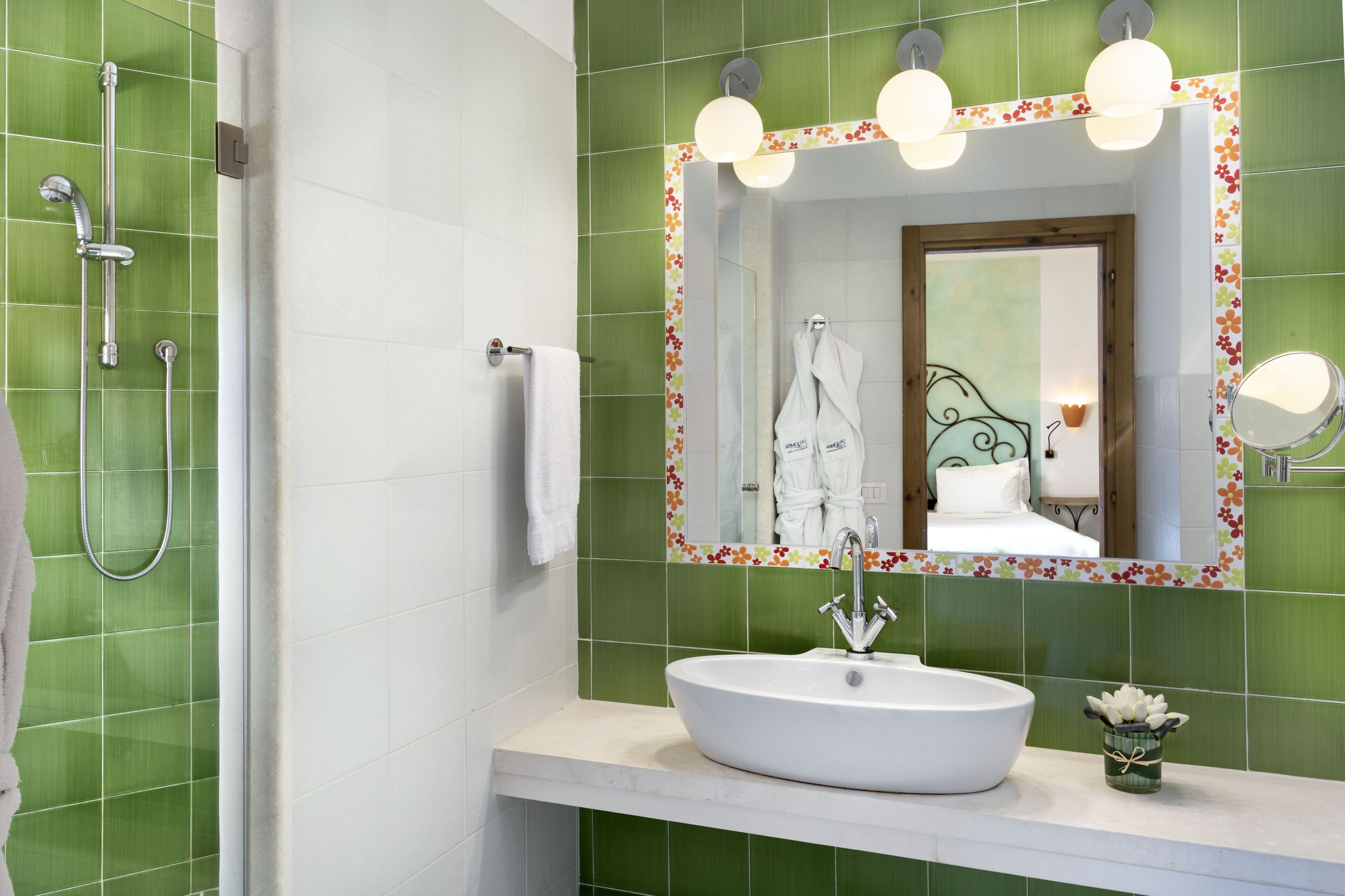 A bathroom with a white sink, green tiles, a shower, and a mirror with lights.